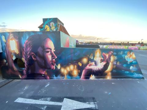 Mural of a woman with a match in her mouth and a candle in her hand. Landscape format. On the ramp of a carpark. 